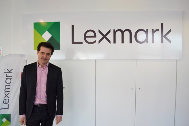 Renaud Deschamps, directeur général de Lexmark en France, pose devant le nouveau logo de la firme, affirmant son virage stratégique dans le logiciel. 